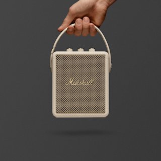 A hand holds Marshall Stockwell III Cream portable speaker.