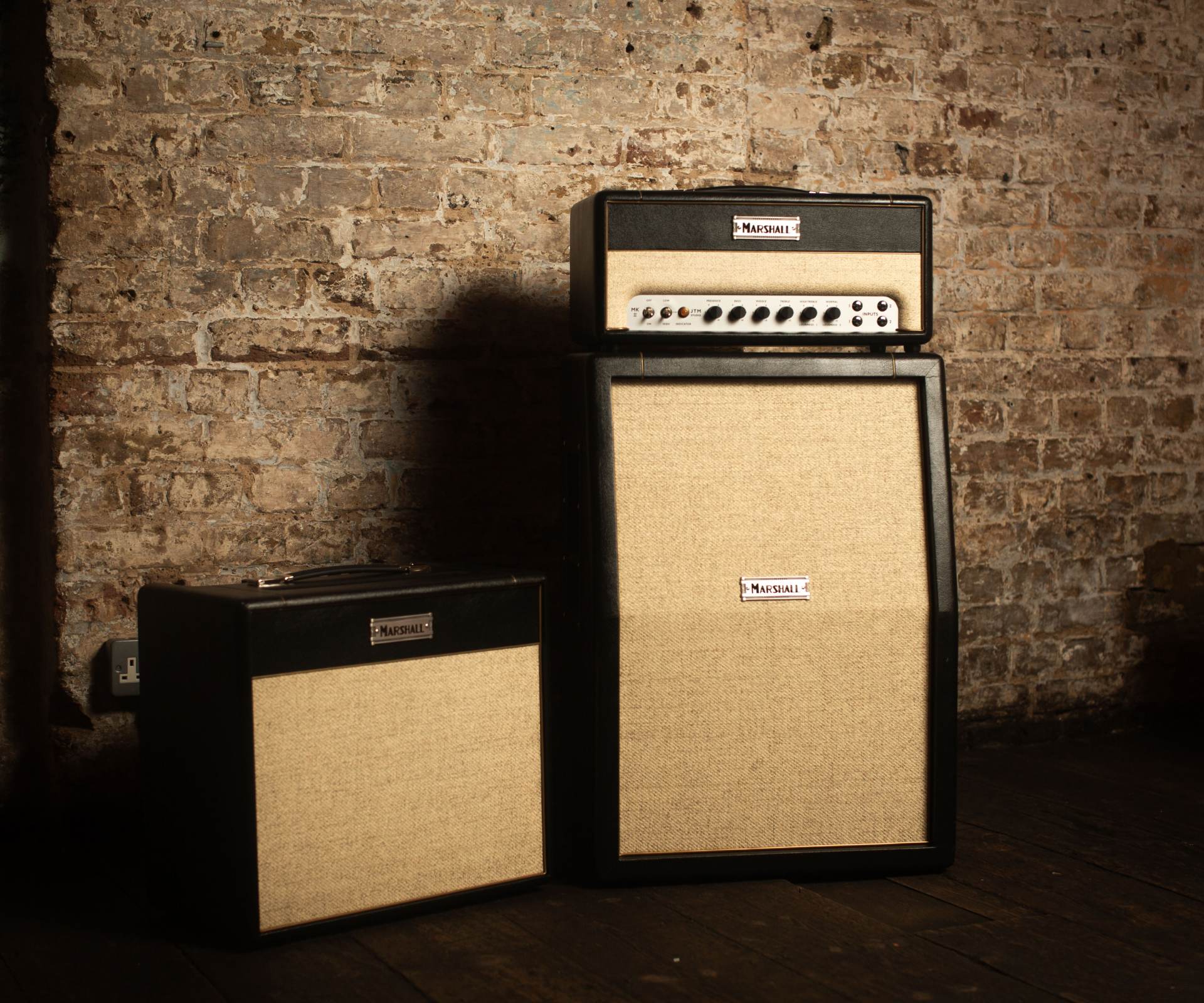 A guitar amplifier stack consisting of a head and a large speaker cabinet placed next to a smaller combo amplifier, set against a brick wall.