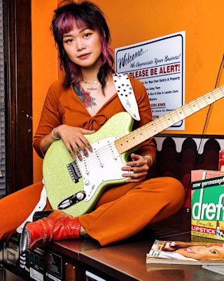 Yvette Young sat on top of a washing machine holding her guitar in a laundrette