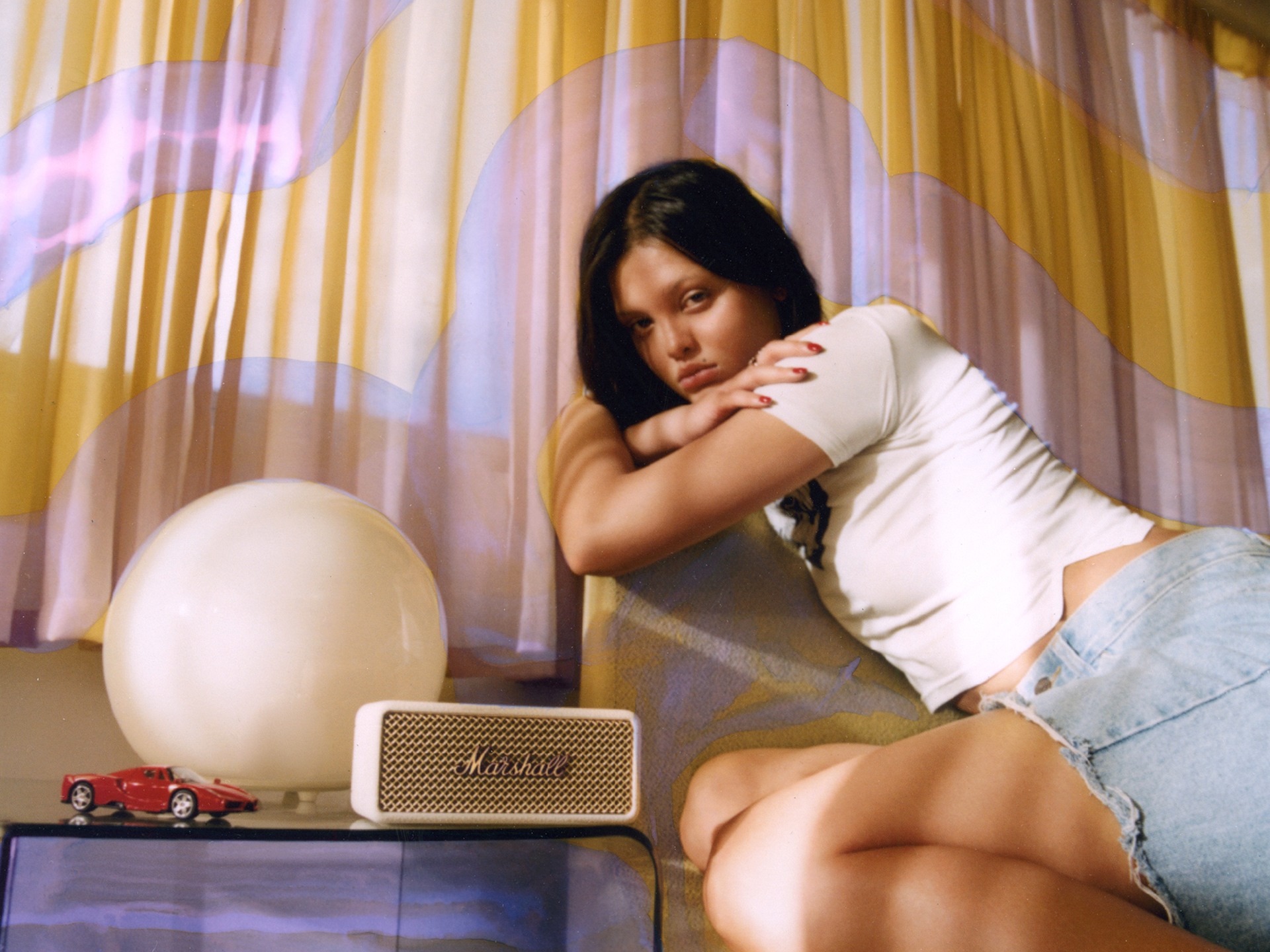 Suki sits on a couch next to Marshall Emberton III Cream portable bluetooth speaker.