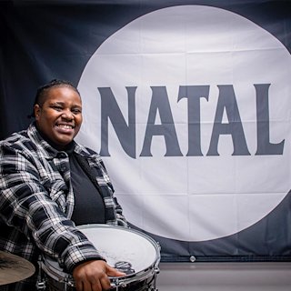 Hannah Montrose posing in front of the Natal drums logo