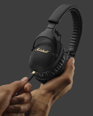 Una mano sosteniendo un par de auriculares Monitor III A.N.C. e insertando un cable de carga USB-C.