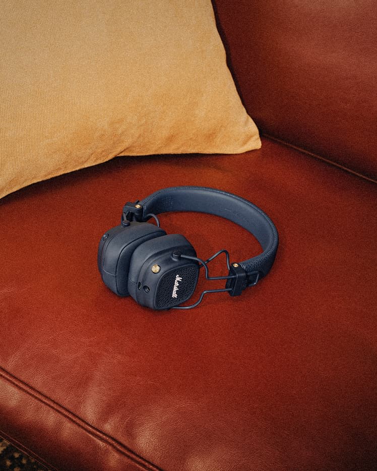 Major V Midnight Blue Bluetooth-Kopfhörer liegen auf einer braunen Ledercouch neben einem hellbraunen Kissen.