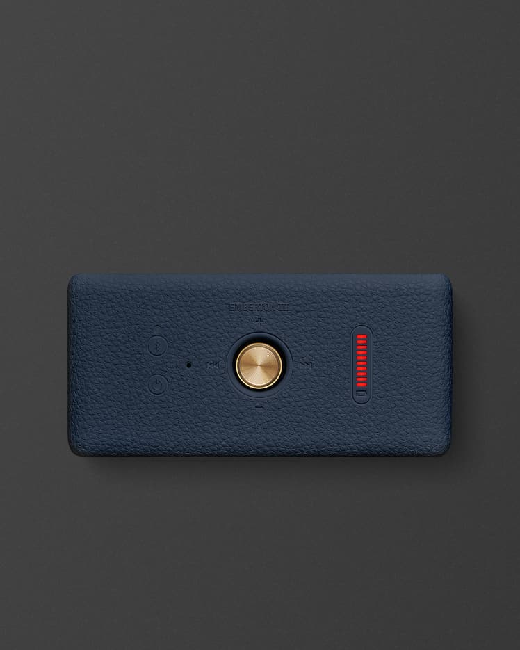 Marshall Emberton III Midnight Blue portable speaker with a textured dark blue surface, featuring a central gold button, two smaller buttons, and a red digital display on a black background.