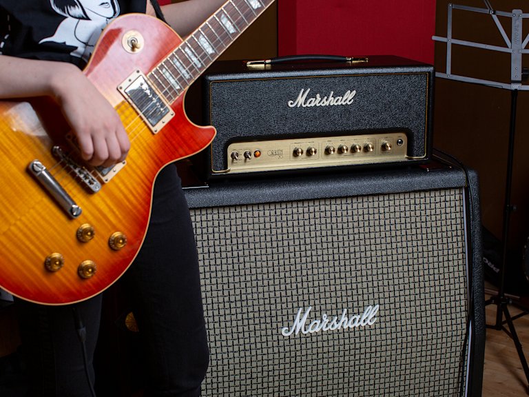 Una guitarra roja conectada al cabezal Origin20 colocado encima de un recinto Marshall