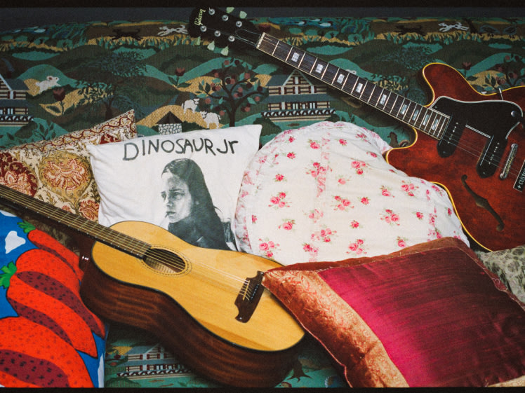 A guitar, and a pillows on a bed.