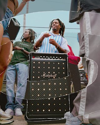 A group of people gather outdoors around the Marshall Bromley 750 party speaker.