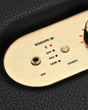 The AUX port, source indicator and source button on the top panel of a Marshall Woburn III speaker.