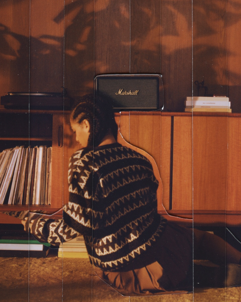 A woman is peacefully laying on the floor in front of a bookcase, immersed in her favorite novel and listening to soothing music through a Marshall STANMORE III speaker.