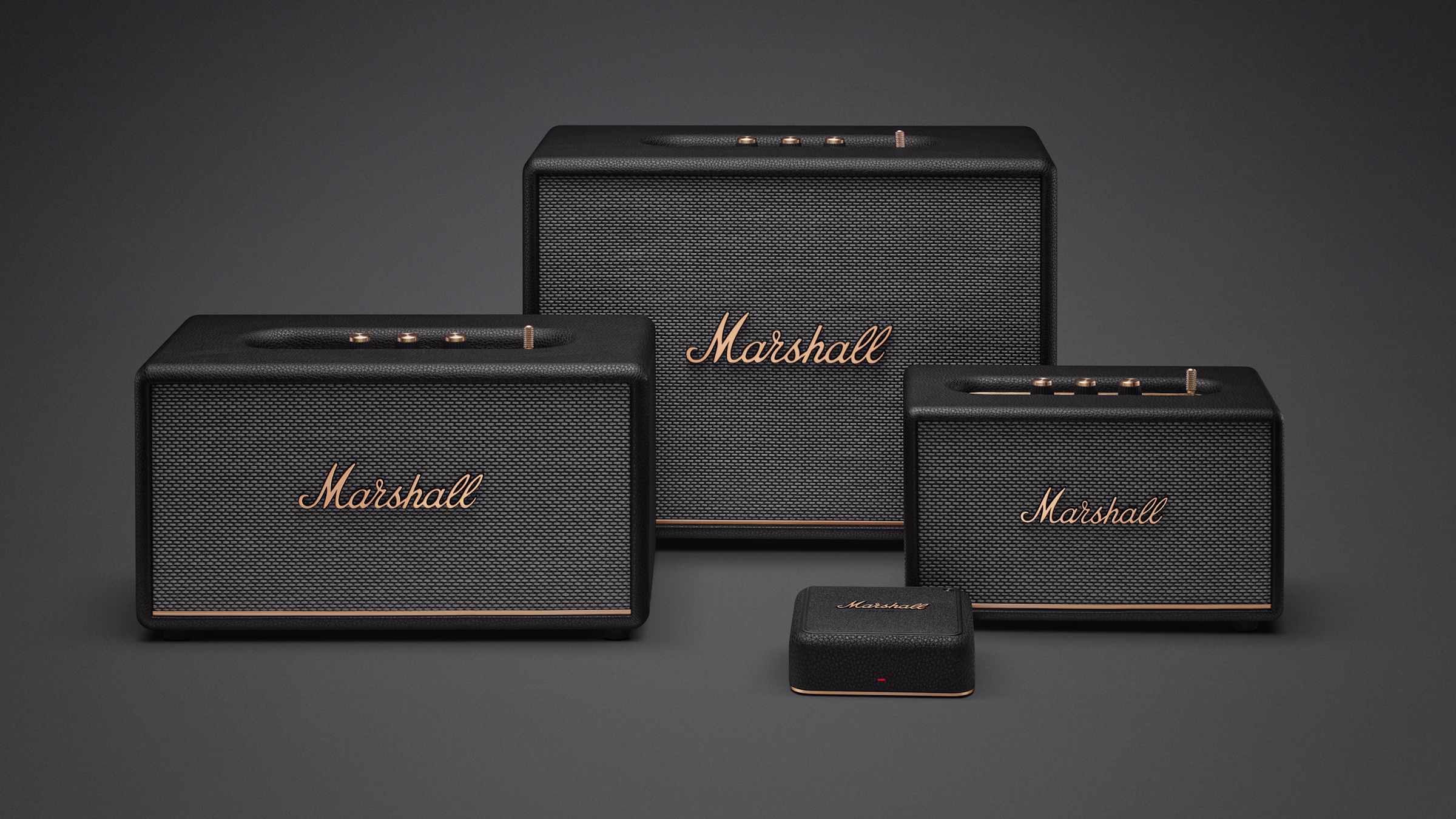 Three black Marshall speakers and Heddon displayed on a gray surface against a gray background.