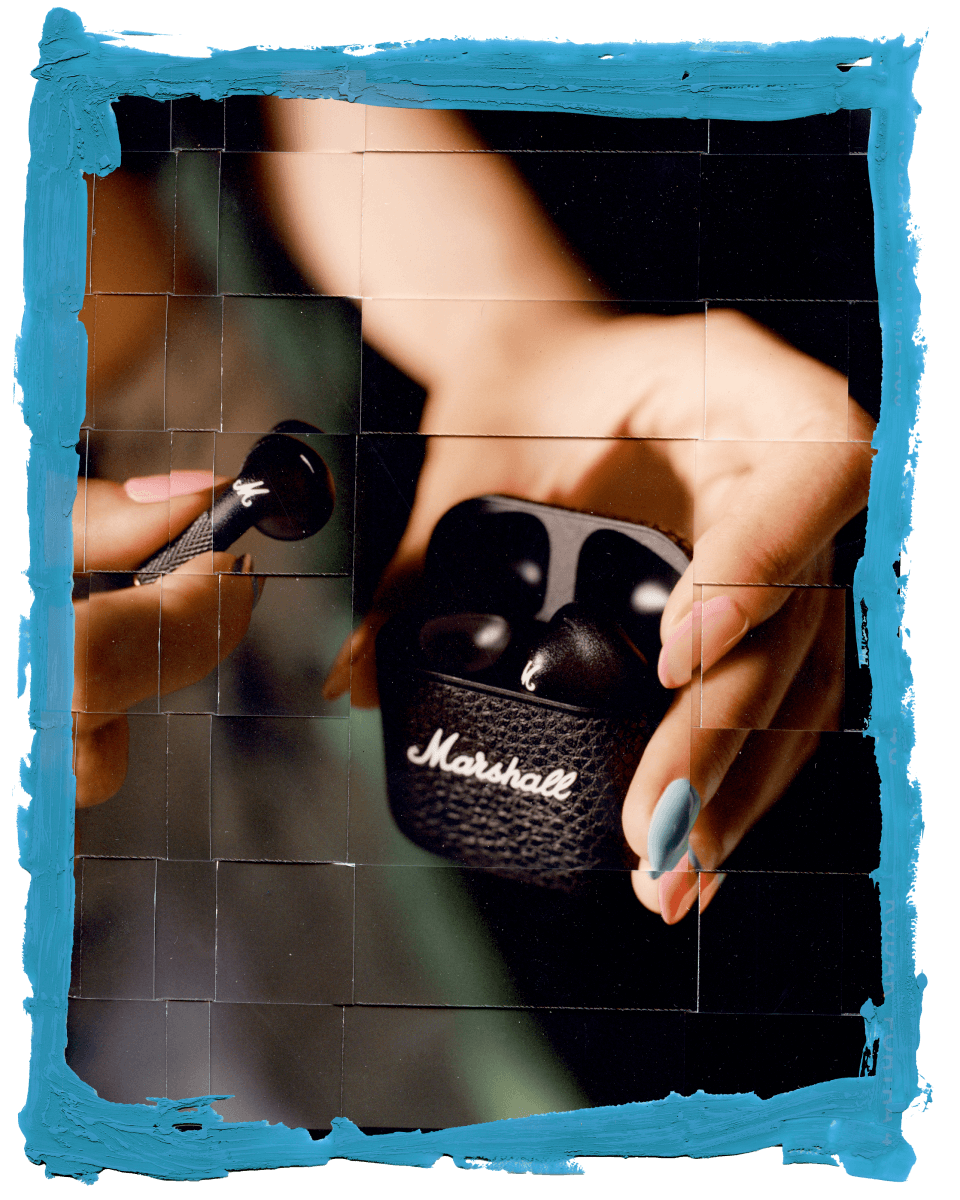 Woman holding a pair of Marshall Minor IV Black true wireless earbuds in a charging case.