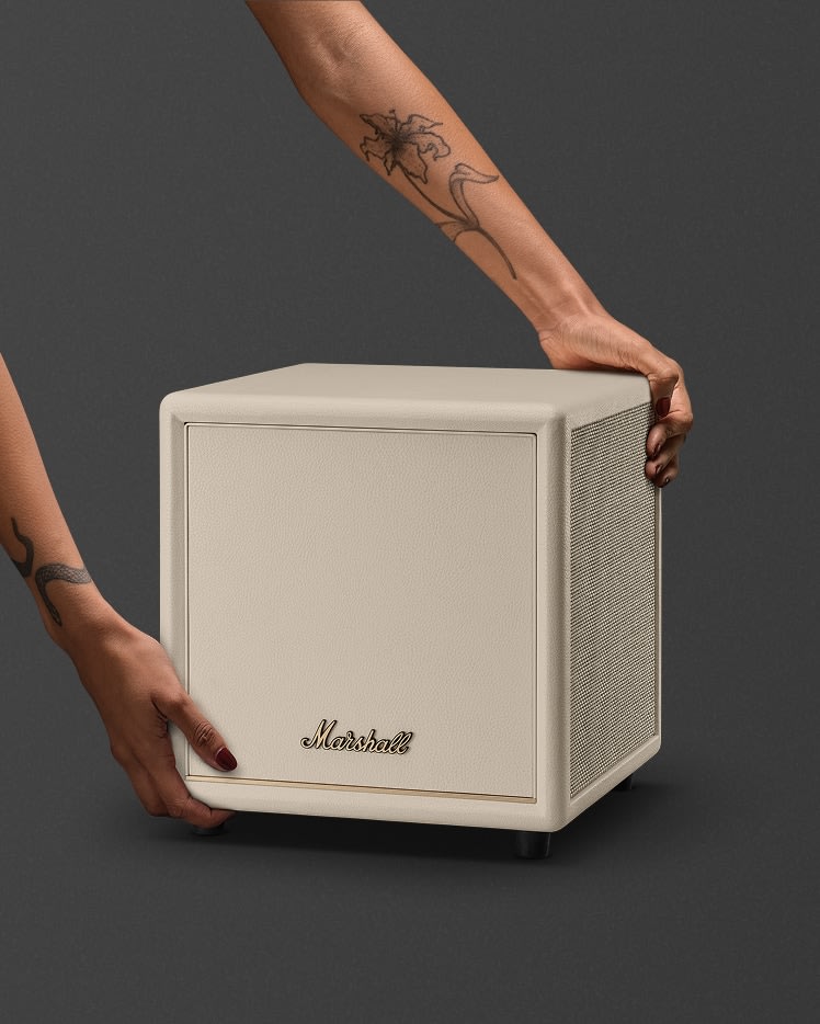 A tattooed individual places a Marshall Heston Sub 200 Cream on a dark surface.