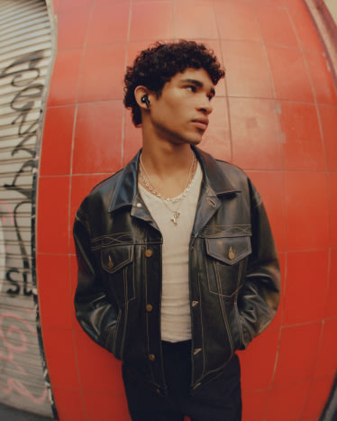 A young man in a Marshall leather jacket standing in front of a red wall.