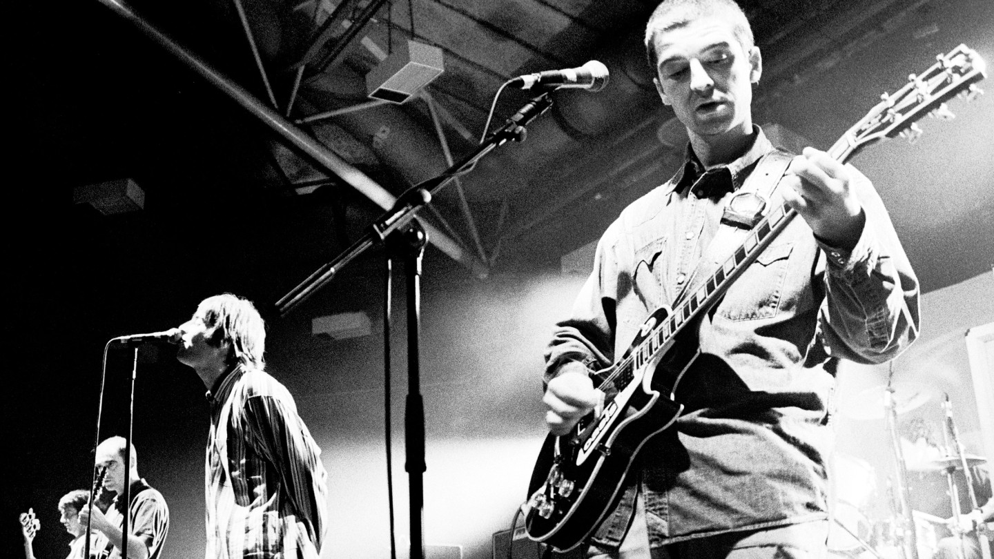 Black and white image of Oasis performing on stage in 1994.