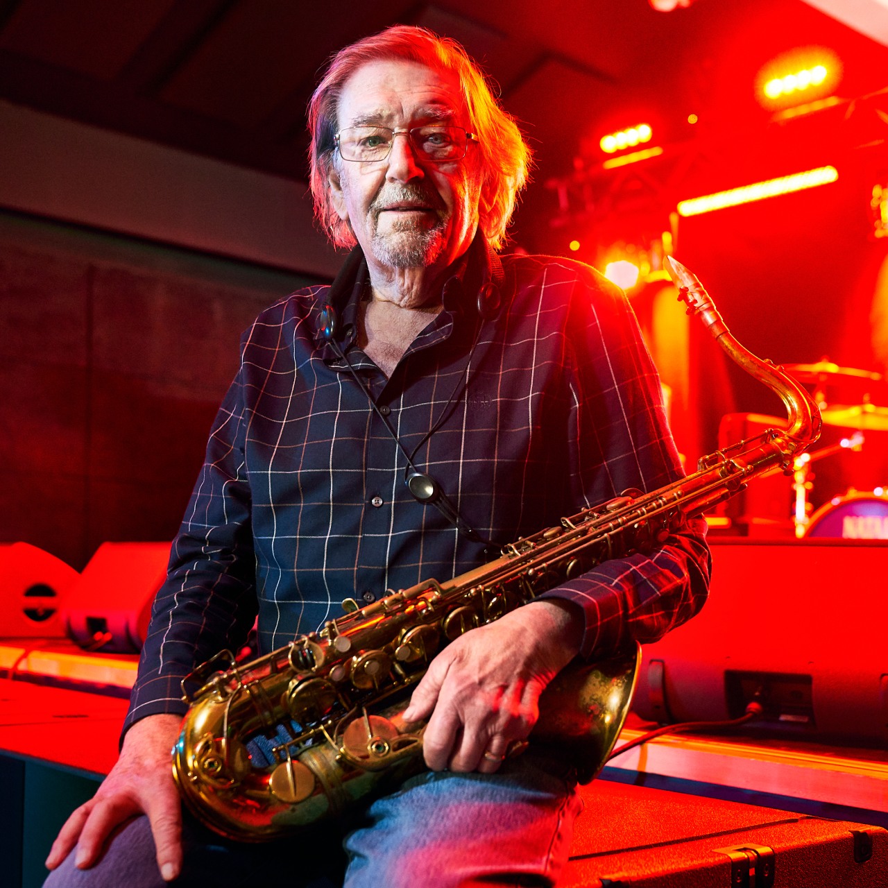 Terry Marshall sits on a stage holding a brass saxophone.