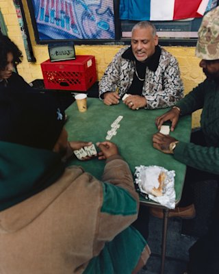 Four people are seated around a table playing dominoes, with the limited-edition Marshall Acton III Awake NY Edition bluetooth speaker providing the perfect background music.