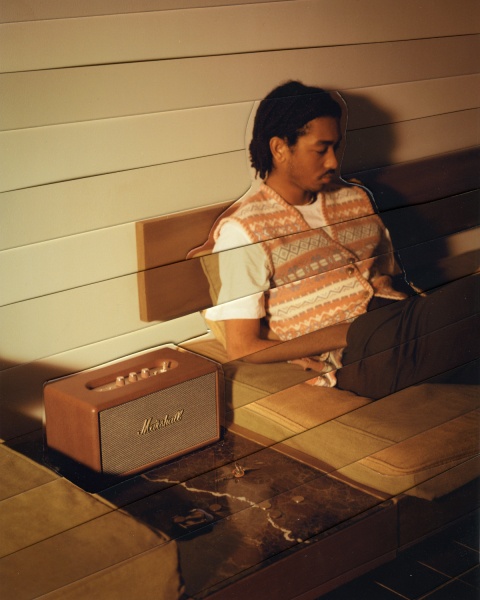 A man sitting on a bed next to a Marshall STANMORE III speaker.