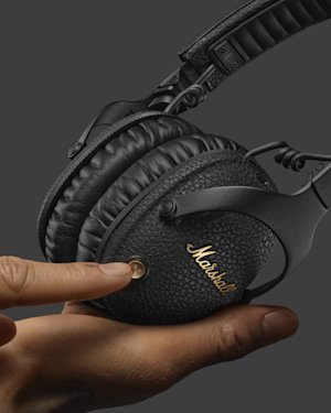 Hands holding a pair of Monitor III A.N.C. headphones and pressing the control knob.