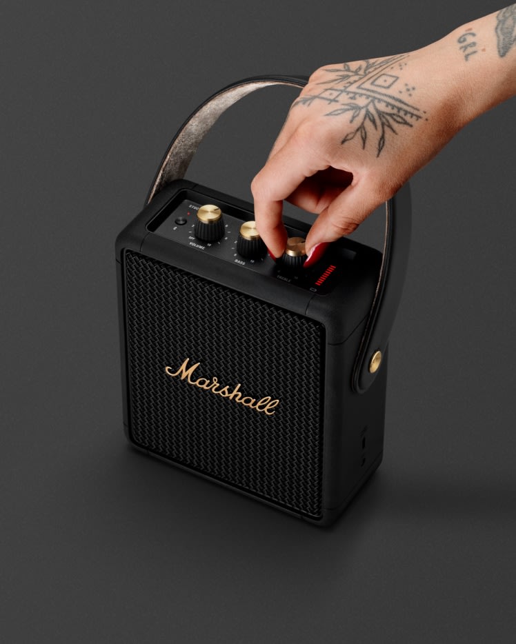 A person changing the volume of a Marshall Stockwell II Black and Brass portable speaker