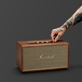 A brown Marshall Stanmore III Bluetooth speaker with control knobs on top, shown against a plain dark background.
