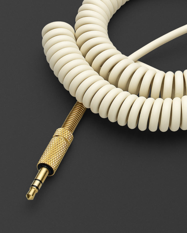 Un cable de audio de altavoz blanco y dorado, denominado también cable Marshall, enrollado cuidadosamente sobre una superficie negra.