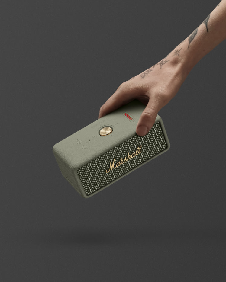 A hand holding a Marshall Emberton III Sage portable Bluetooth speaker against a dark background.