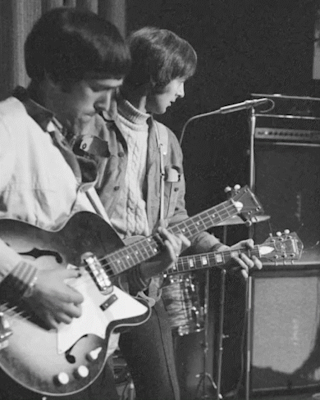 Gif en blanco y negro de un grupo tocando la guitarra con amplificadores Marshall de fondo.