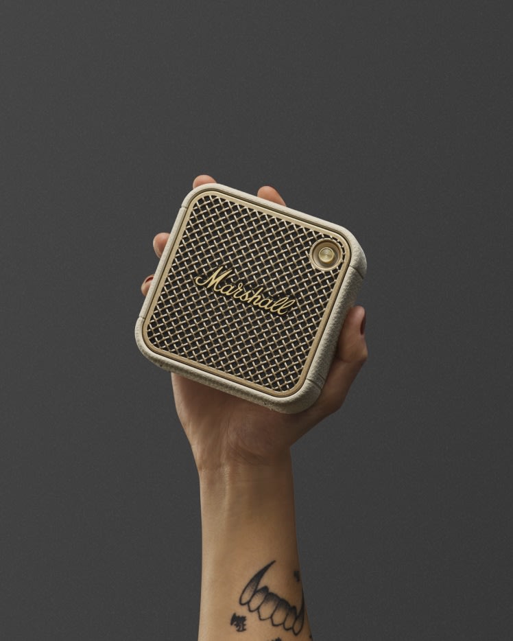 A person holding a Marshall Willen II Cream bluetooth speaker with a mesh front.