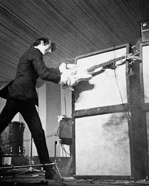 A man in a suit playing a guitar on stage.