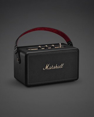 The Marshall Kilburn III Black and Brass portable speaker, featuring a red handle, gold control knobs, and the iconic logo on the front grille, is displayed against a dark background.
