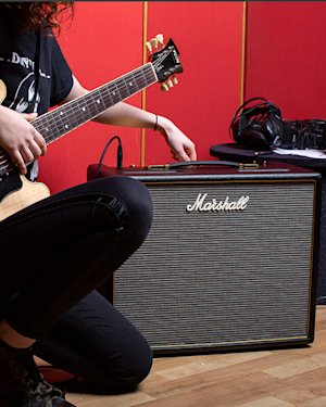 A guitarist adjusting the treble from his combo amplifier by Marshall