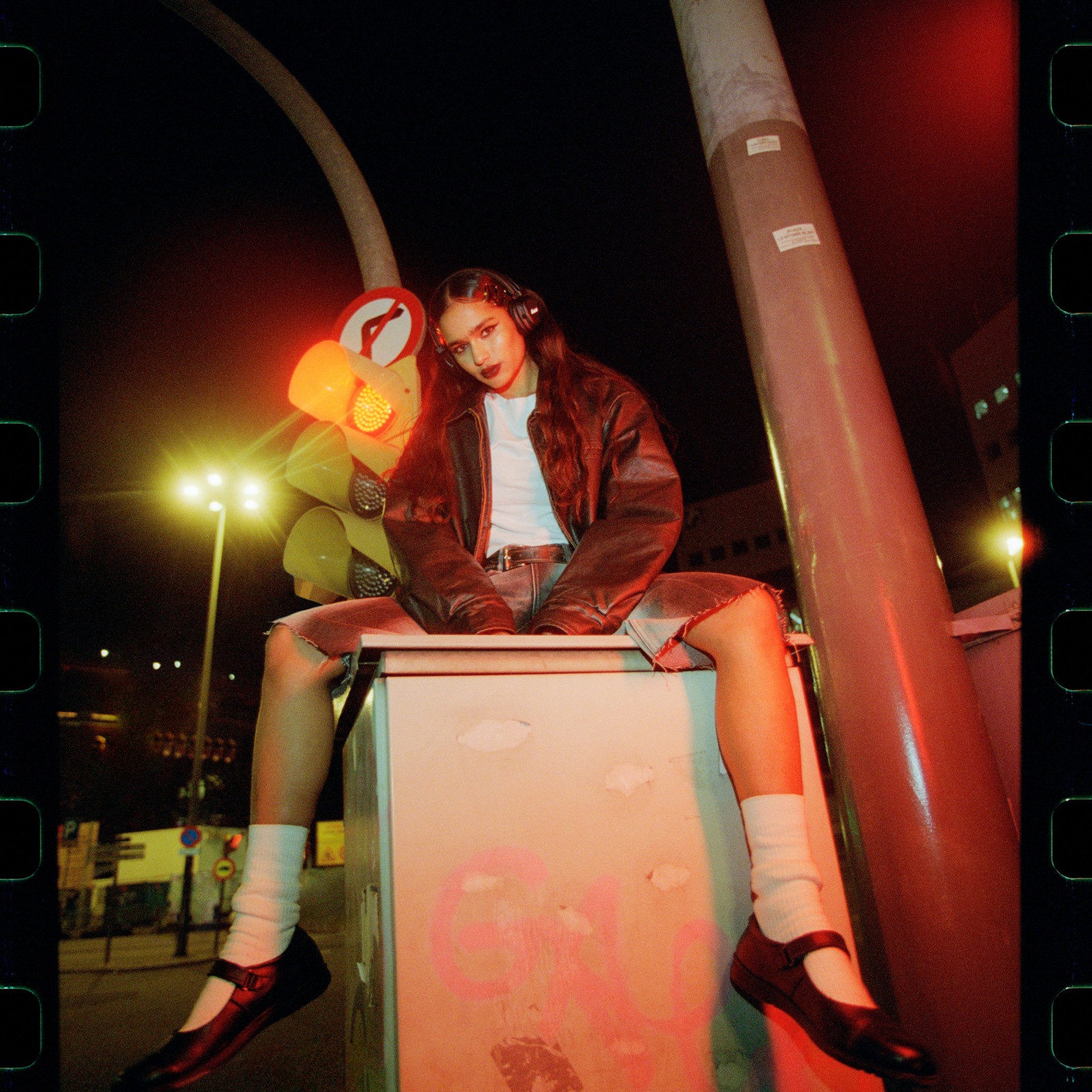 Woman sitting at night with a streetlight in the background, wearing Marshall Major V Black on-ear headphones.