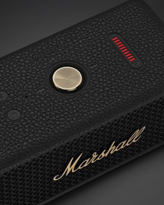 Close-up of a Marshall Emberton III Black and Brass Bluetooth speaker with a central gold control knob, power button, and volume indicator bar.