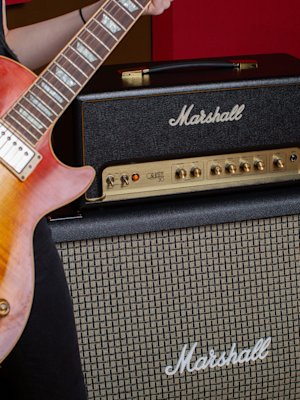 A woman is playing a guitar with a Marshall Origin50 Head amplifier.