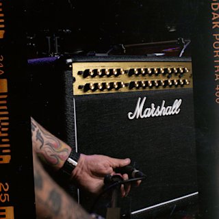 A man with a tattoo on his arm is playing a guitar using a Marshall JVM410 Combo amplifier.