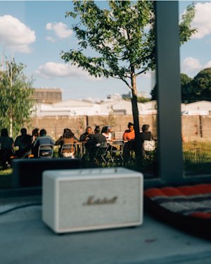 People from Roots Berlin sitting together at the background of a image with Blurred Marshall Cream Speaker on a table.