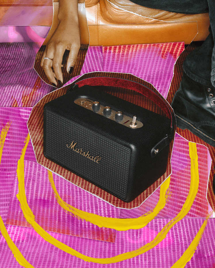 Marshall Kilburn III Black and Brass portable speaker on a textured pink and yellow surface.