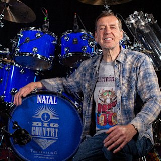 Mark Brzezicki posing next to a blue Natal drum
