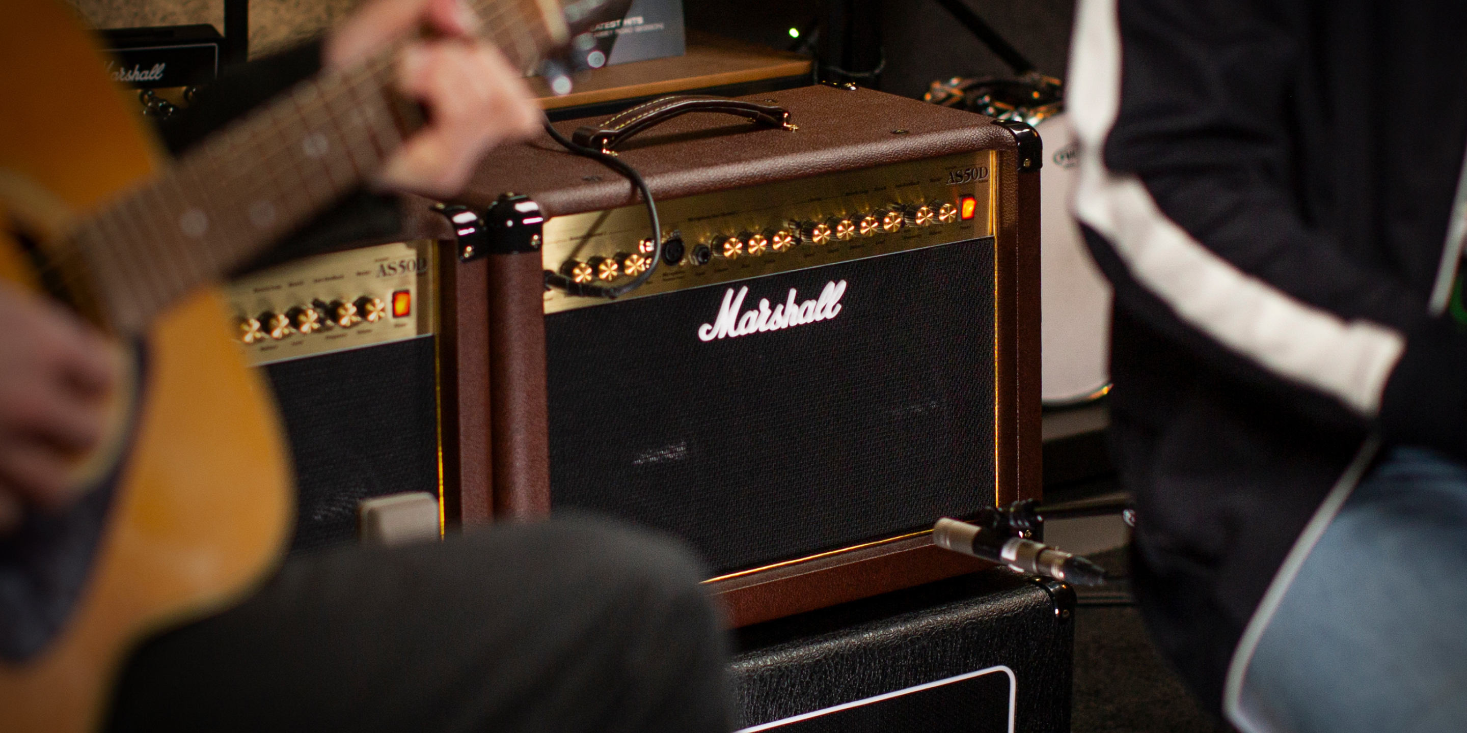 A person playing guitar near a Marshall AS50D acoustic amplifier.