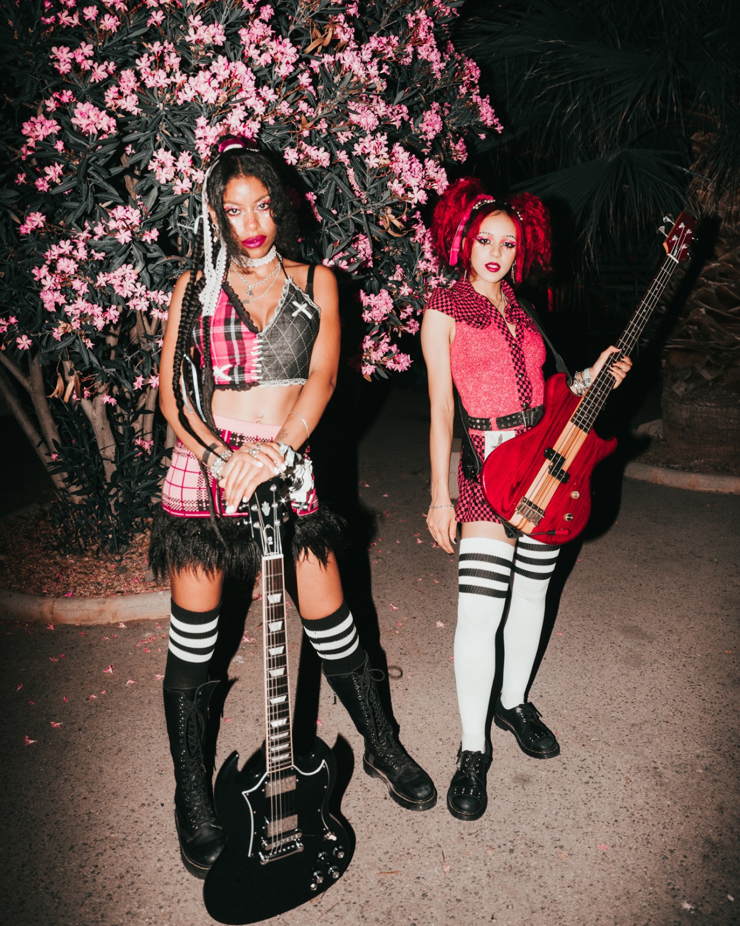 Two stylish musicians from Nova Twins posing in front of a tree full of pink flowers.