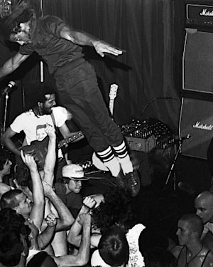 Black and white photo of a musician jumping in the crowd with Marshall amplifiers in the stage.