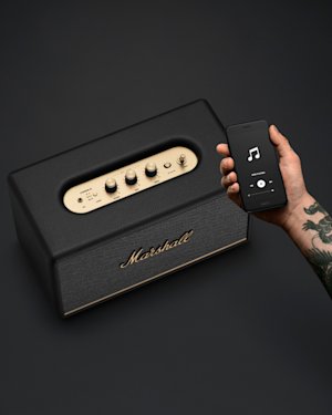 A tattooed hand holding a phone over a Stanmore III speaker.