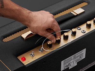 A person is adjusting the knobs on a Marshall 1974X guitar amplifier.