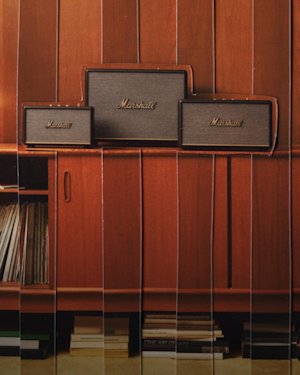 Drei Marshall-Heimlautsprecher stehen auf einem Holzschrank, darunter befinden sich Regale mit Schallplatten und Büchern.