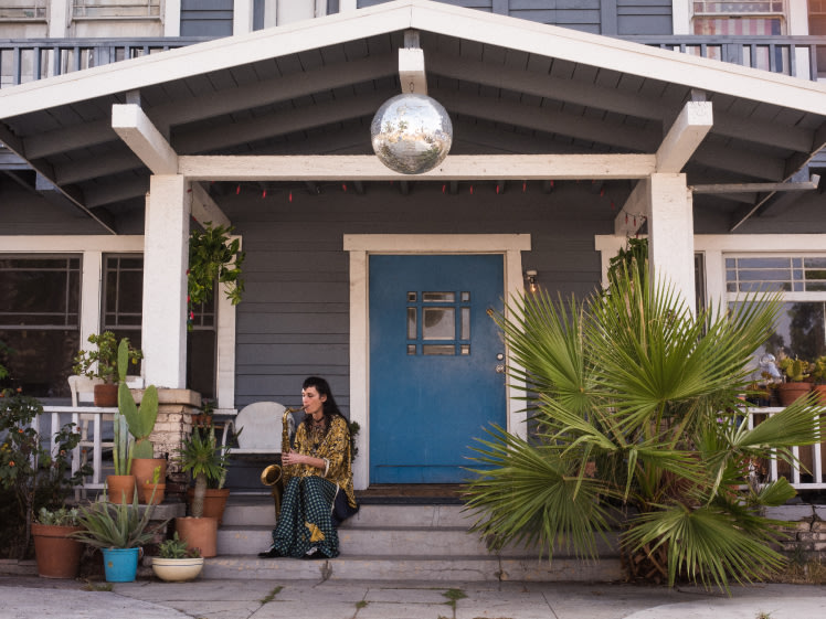 Zumi Rosow sitting on the steps of a house playing a saxophone.