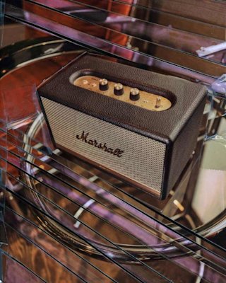 Ein Marshall-Verstärker steht auf einem Glastisch mit einem Schlagzeug im Hintergrund, auf dem die Knöpfe und das Lautsprechergitter zu sehen sind.
