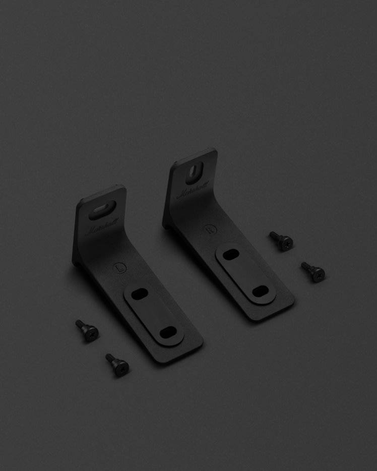 Los soportes de pared Heston 120 de Marshall, etiquetados como "L" y "R", se colocan uno al lado del otro con tornillos a juego cerca sobre una superficie oscura.