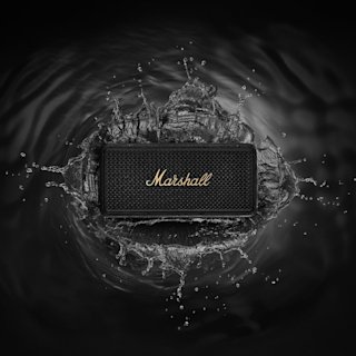 Marshall Middleton II Black and Brass portable Bluetooth speaker sits at the center of a splash of water against a dark background.