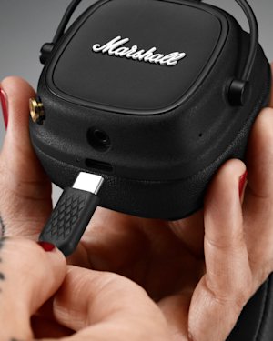 A hand with tattoos holding a pair of Major IV headphones, putting a charging cable into them.