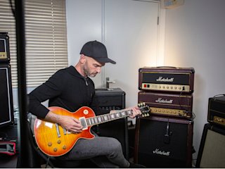 Man with cap playing a guitar surrounded by Marshall amps